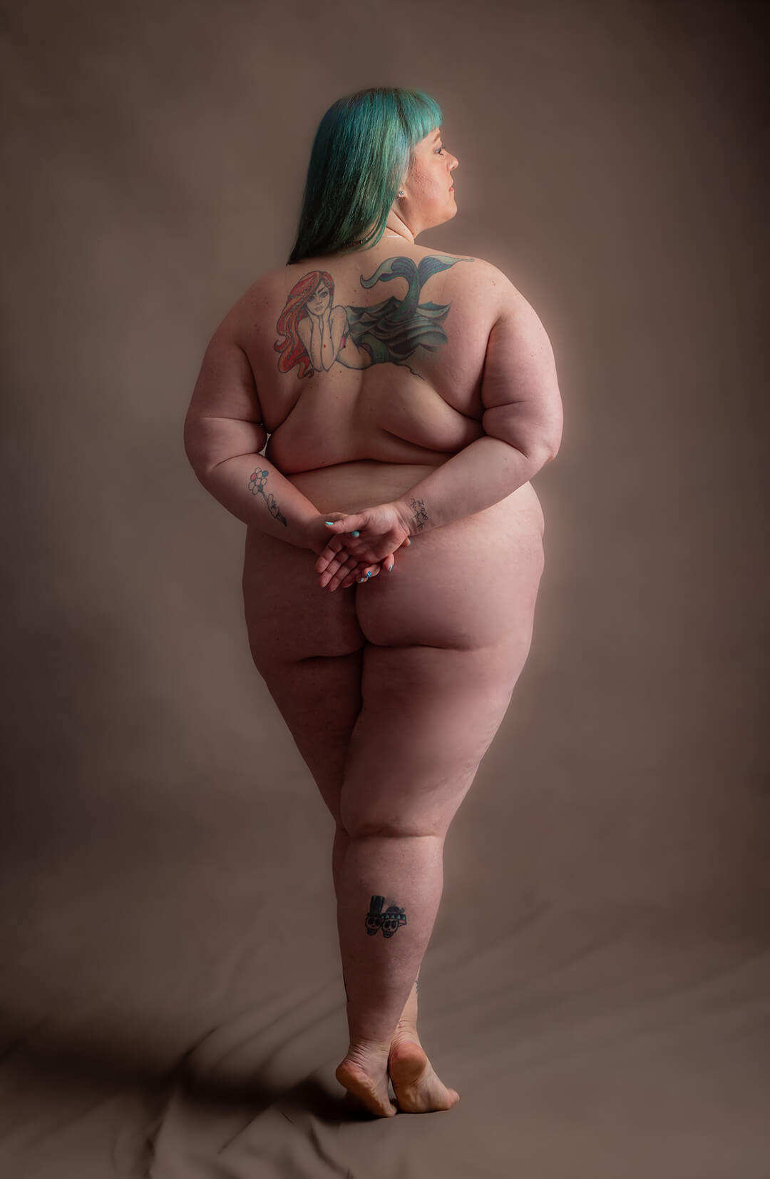 Gently coloured photograph of a person with a mermaid back tattoo and green hair photographed artisticaly and beautifully lit